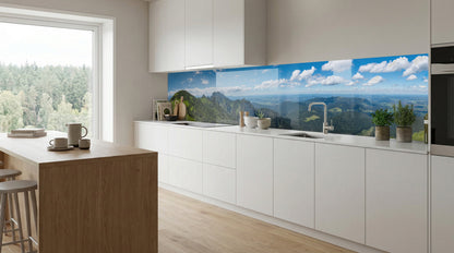 Moderne weiße Küche mit einer Küchenrückwand „Berglandschaft“ von glasposter.com und einem großen Fenster mit Blick auf den Wald.