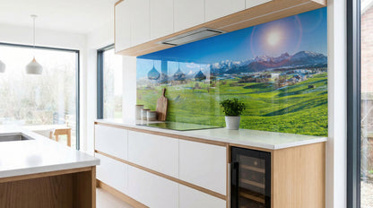 Moderne Küche mit weißen Schränken und einer Küchenrückwand „Sonnenaufgang Alpenwiesen“ von glasposter.com.