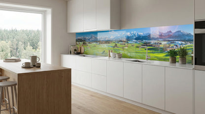 Moderne weiße Küche mit Kücheninsel aus Holz und einer Küchenrückwand mit dem Motiv „Sonnenaufgang Alpenwiesen“ von glasposter.com.