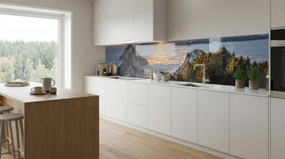 Moderne Küche mit weißen Schränken, Holzakzenten und einer Glasposter-Fliesenwand mit dem Motiv „Sonnenuntergang, Bergsee, Wald“.