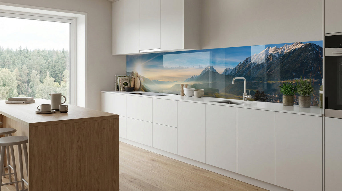 Moderne weiße Küche mit großem Fenster und dem Küchenspiegel „Alpenpanorama Schneegipfel“ von glasposter.com.