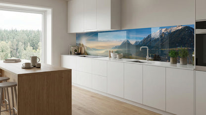 Moderne weiße Küche mit großem Fenster und dem Küchenspiegel „Alpenpanorama Schneegipfel“ von glasposter.com.