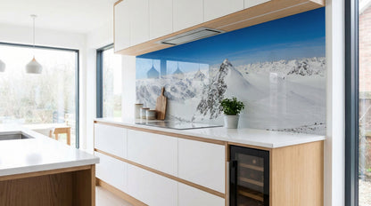 Moderne Küche mit weißen Schränken, einer Küchenrückwand – „Schneebedeckte Berge“ von glasposter.com – und einer Pflanze.